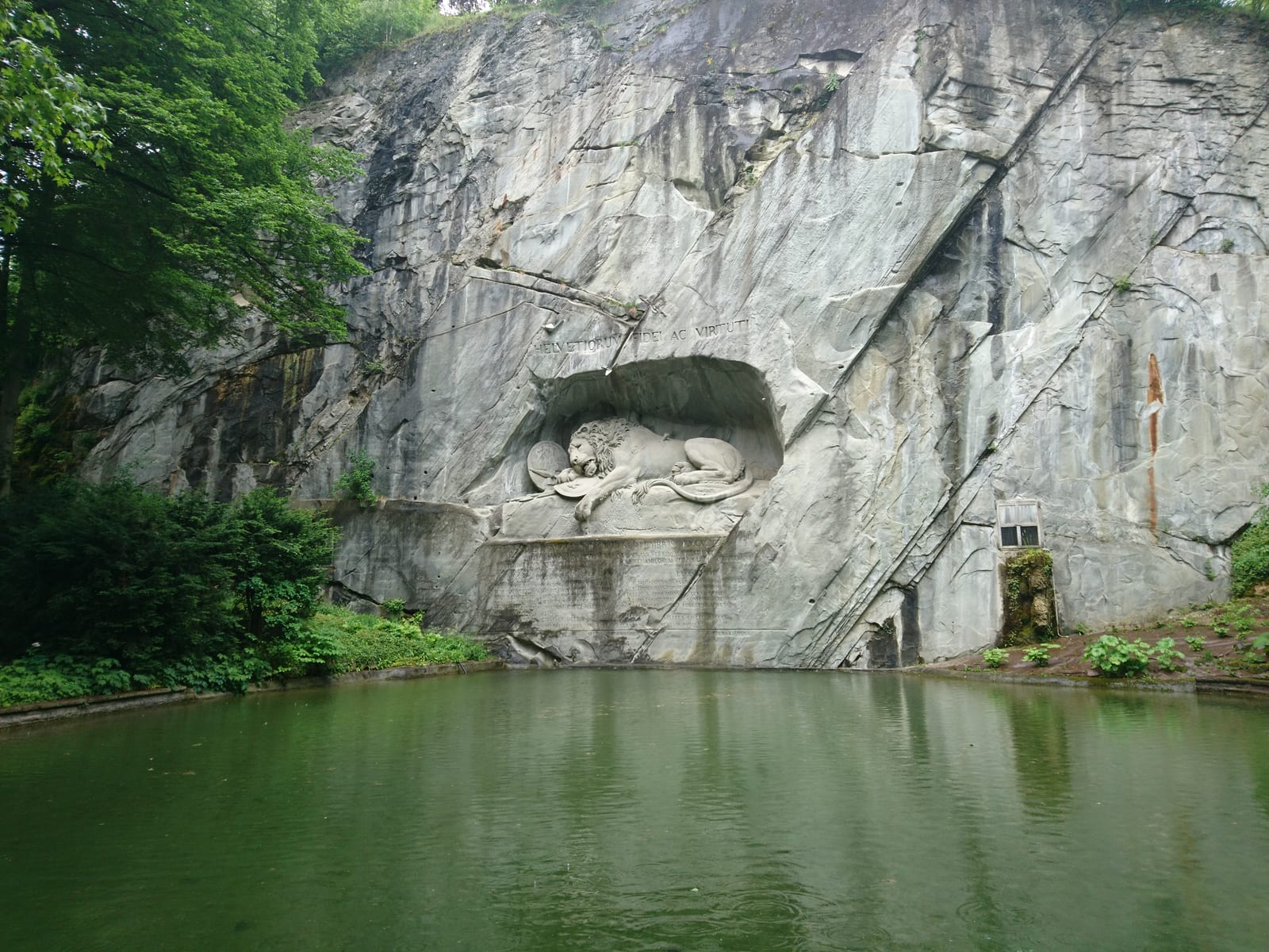 Der sterbende Löwe von Luzern, in eine Felswand gehauen, davor der stille Teich im Grünen.
