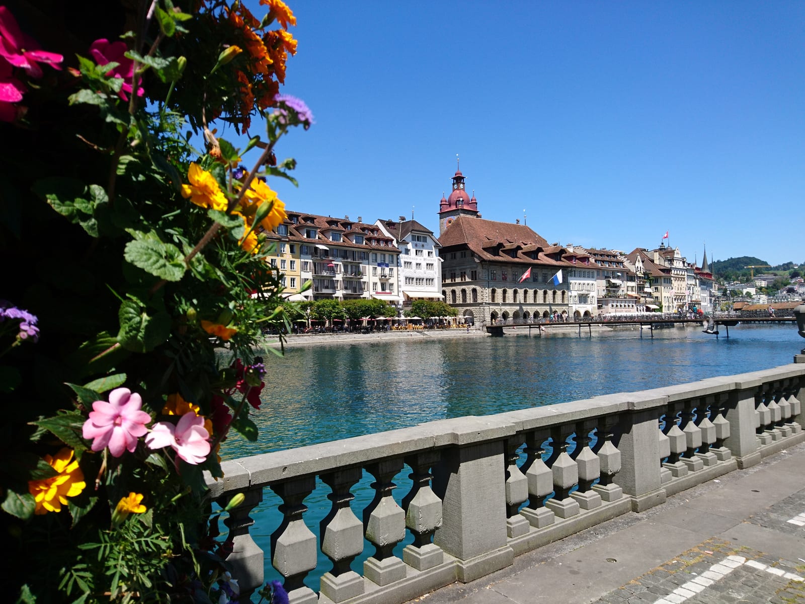 Blumenkästen auf einer Brücke über die Reuss in Luzern, dahinter die Altstadthäuser am Ufer.
